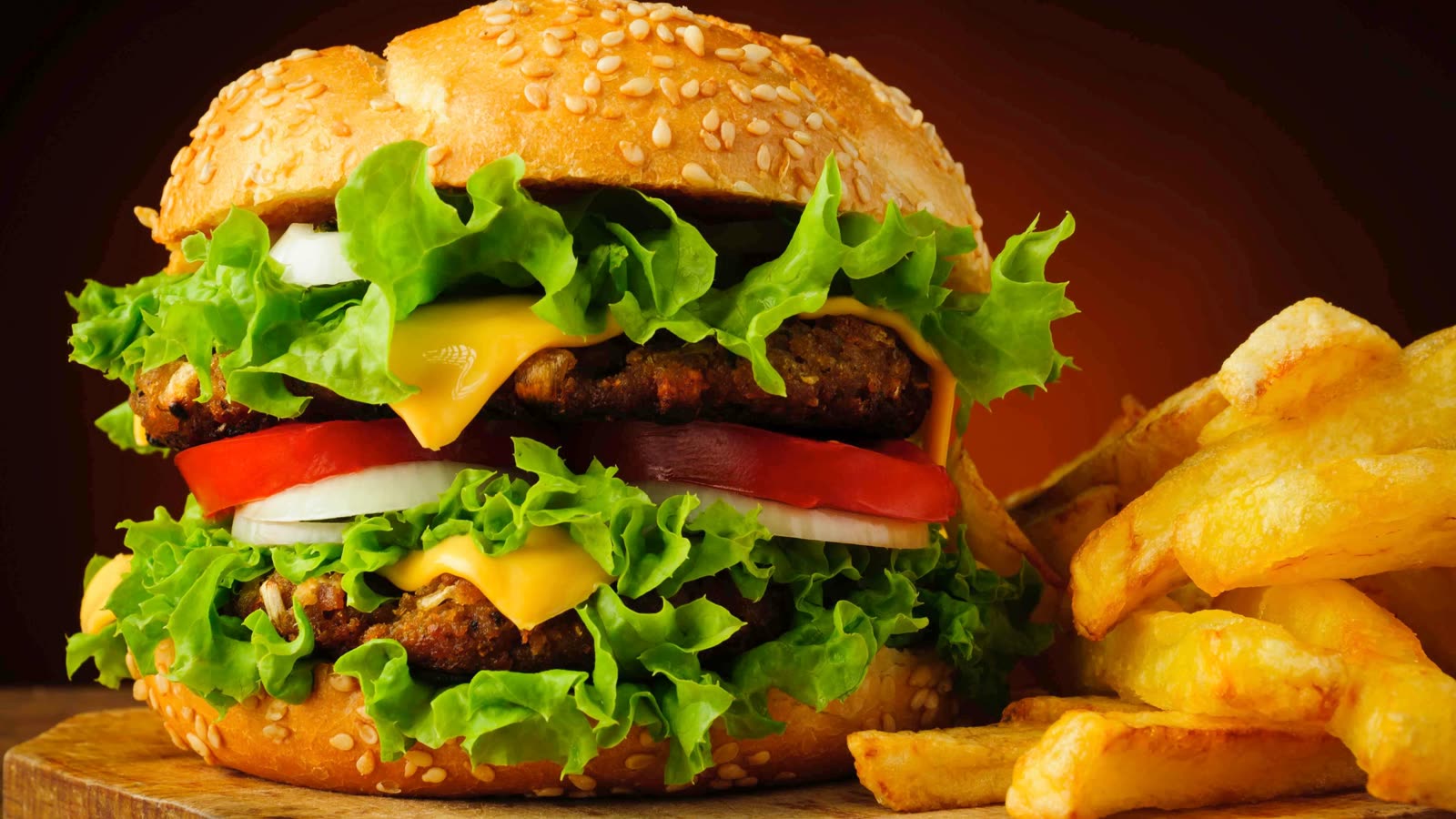 Een dubbele hamburger met sla, tomaat, kaas en een portie frites.